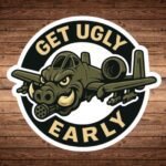 Round Get Ugly Early sticker with an A-10 Warthog jet that has a warthog face, on a wood background