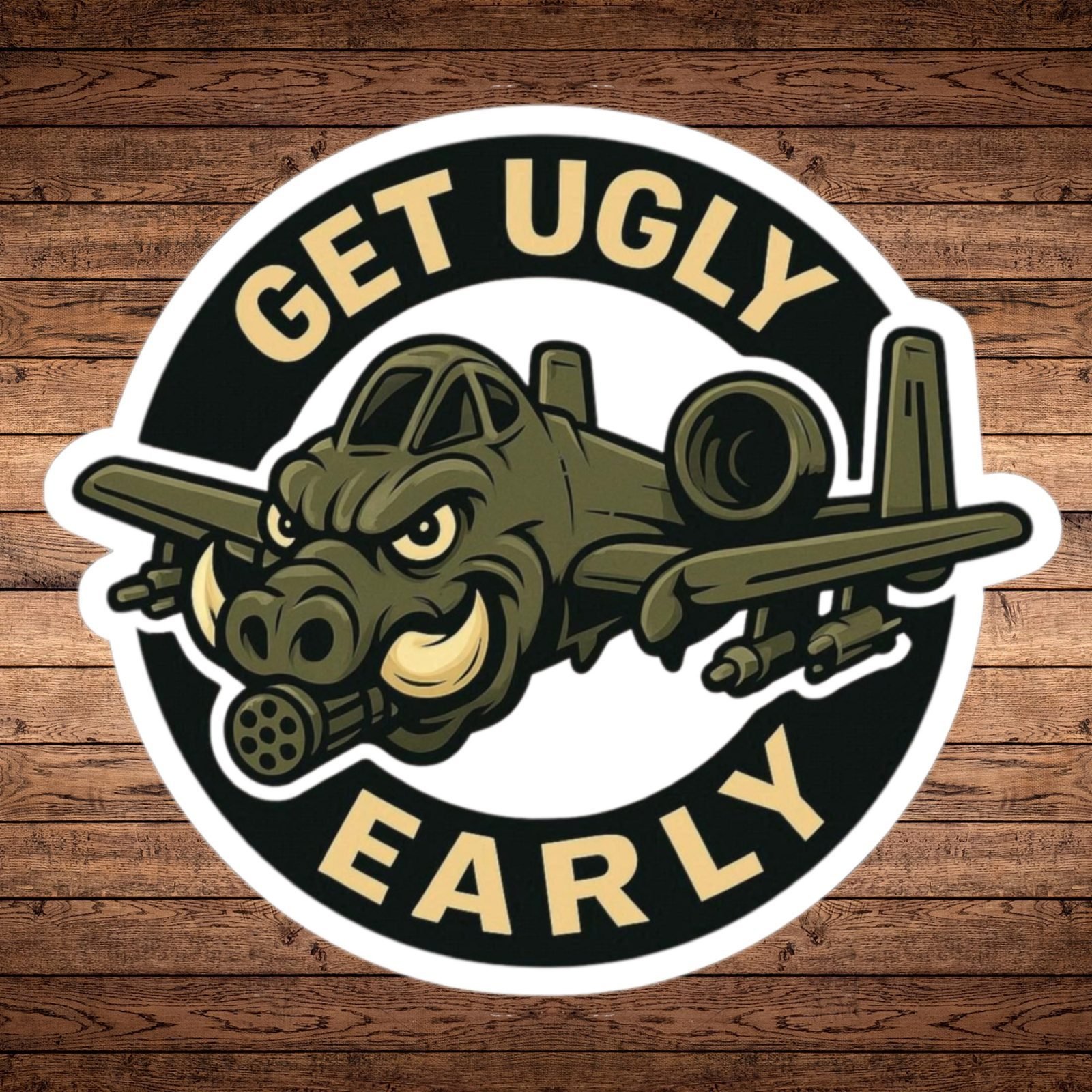 Round Get Ugly Early sticker with an A-10 Warthog jet that has a warthog face, on a wood background