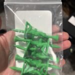 Hand holding a clear bag with five green toy soldier golf tees