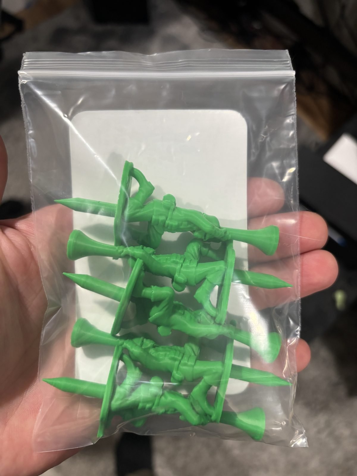 Hand holding a clear bag with five green toy soldier golf tees