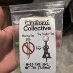 Hand holding a clear bag of army man golf tees with a card reading Hold the Line, Hit the Fairway