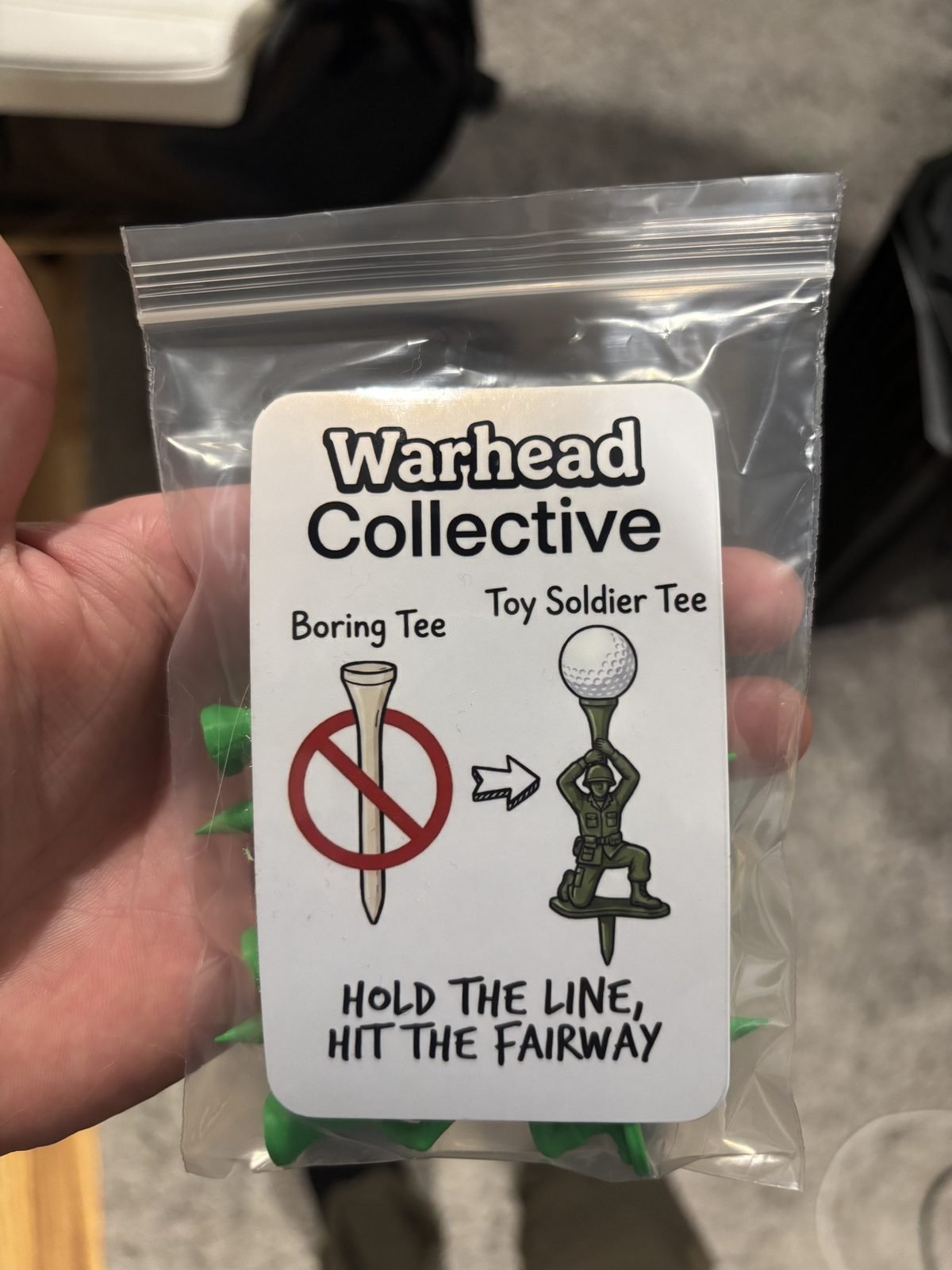 Hand holding a clear bag of army man golf tees with a card reading Hold the Line, Hit the Fairway