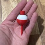 Hand holding a red and white bobber golf tee over a wooden table