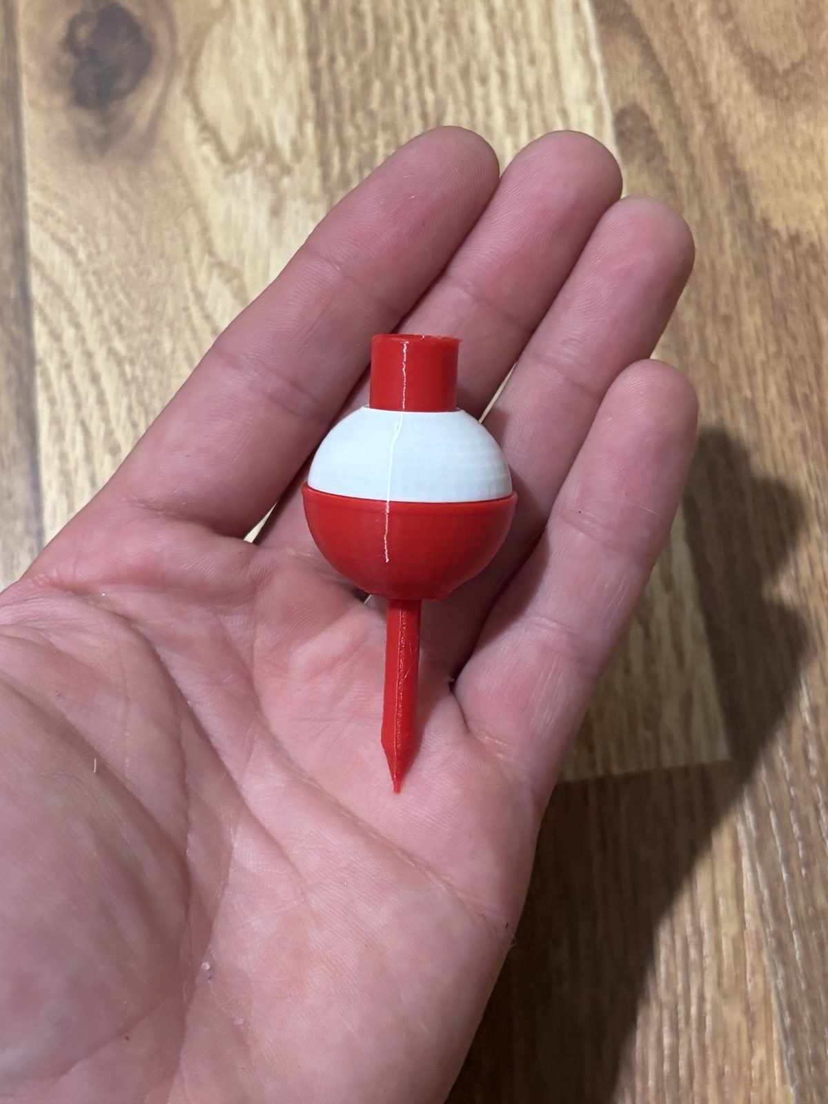 Hand holding a red and white bobber golf tee over a wooden table