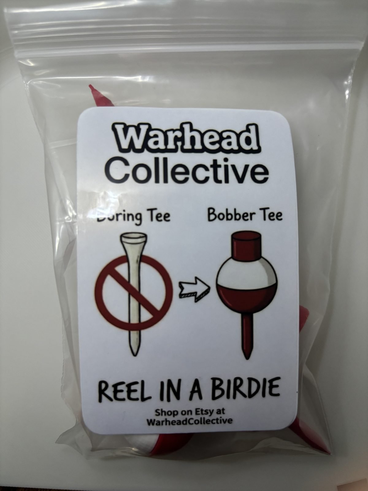 Warhead Collective bag of fishing bobber golf tees with a card reading Reel in a Birdie