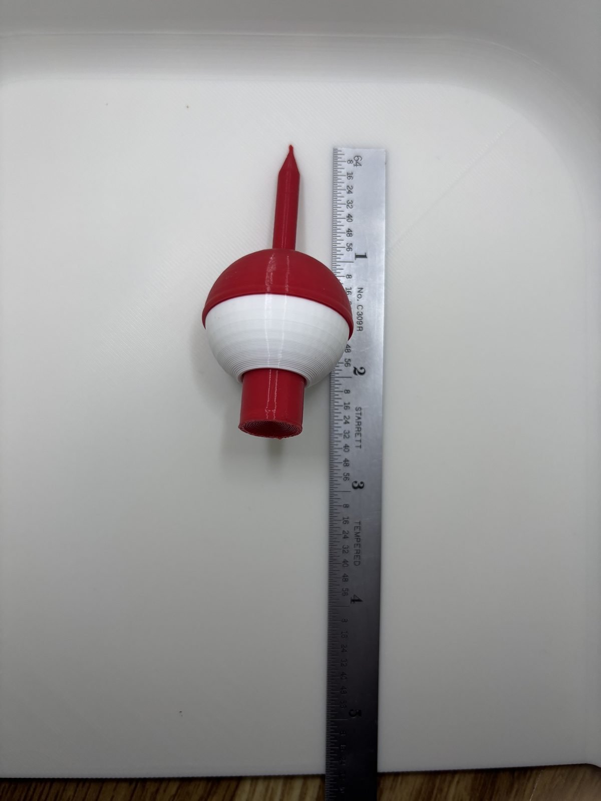 Red and white bobber golf tee next to a metal ruler to show its length