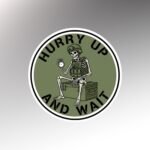 Round olive sticker reading Hurry Up and Wait with a skeleton in a helmet and vest sitting on a crate