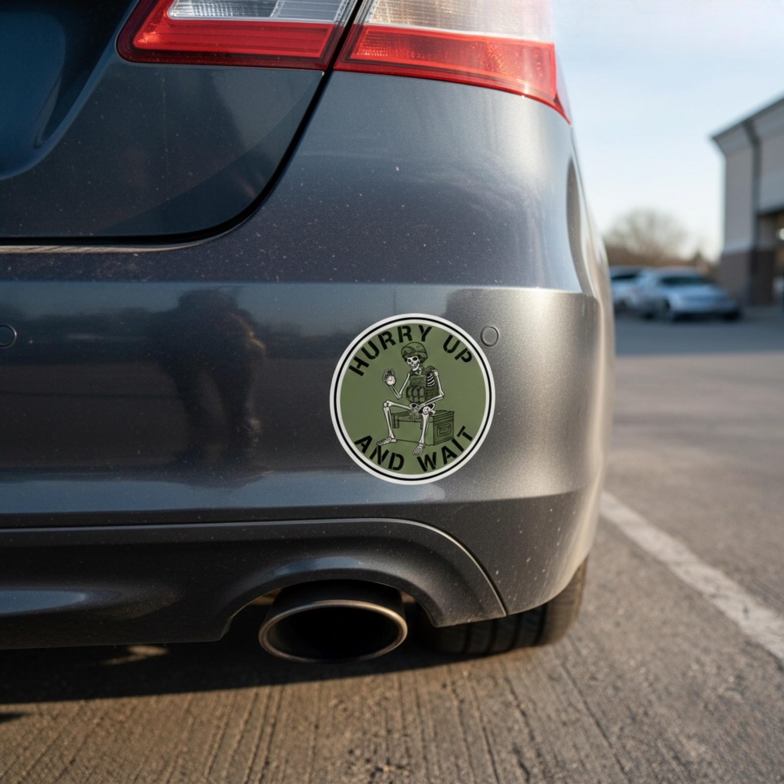 Hurry Up and Wait sticker on the rear bumper of a gray car near the exhaust