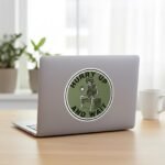 Hurry Up and Wait sticker on a silver laptop lid next to a coffee mug