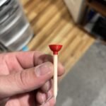 Hand holding a golf tee with a red plunger cup on top