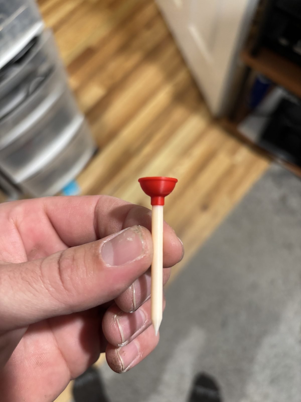 Hand holding a golf tee with a red plunger cup on top