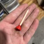 Golf tee with a red plunger cup lying in an open palm
