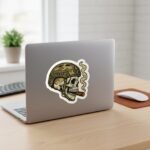 Tactical skull sticker on a silver laptop lid next to a plant and a mouse