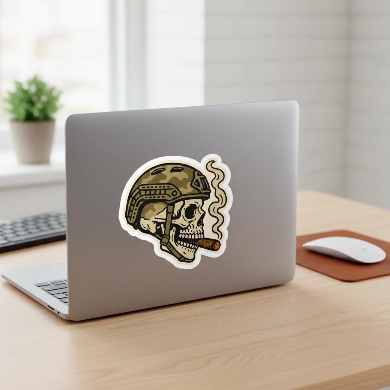 Tactical skull sticker on a silver laptop lid next to a plant and a mouse
