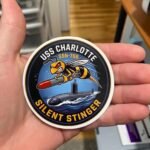 Hand holding the round USS Charlotte Silent Stinger sticker to show its size