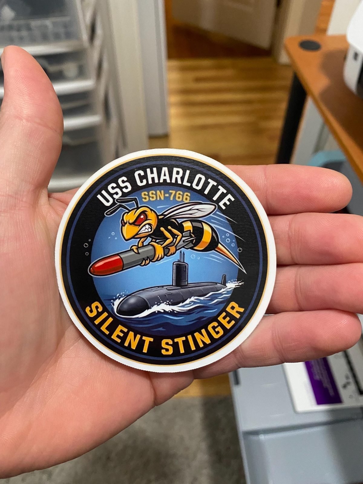 Hand holding the round USS Charlotte Silent Stinger sticker to show its size